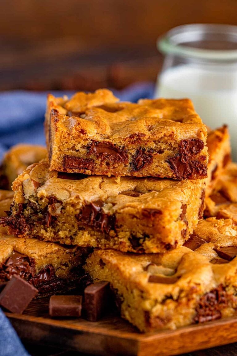 A stack of chocolate chunk blondies showing gooey melted chocolate, next to a jar of milk.
