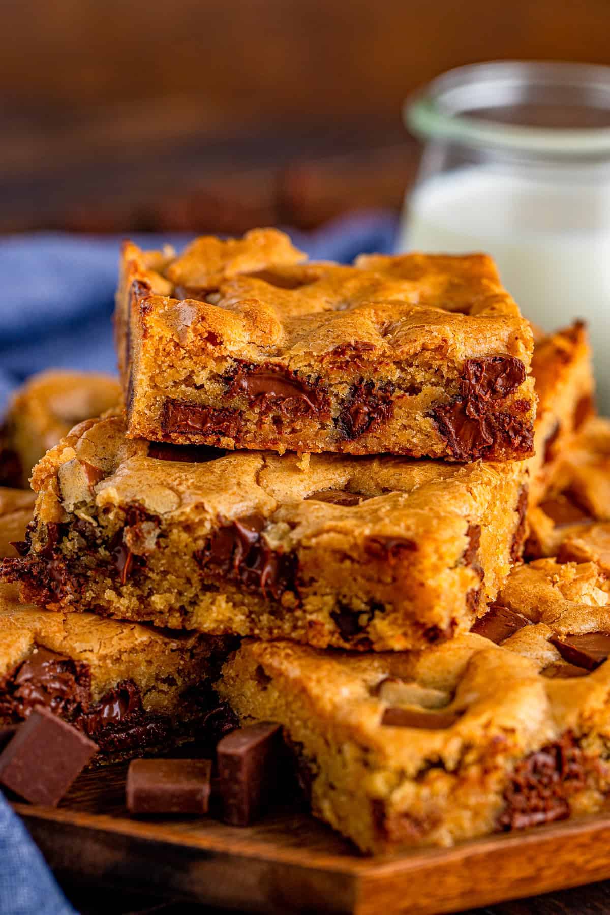 A stack of chocolate chunk blondies showing gooey melted chocolate, next to a jar of milk.