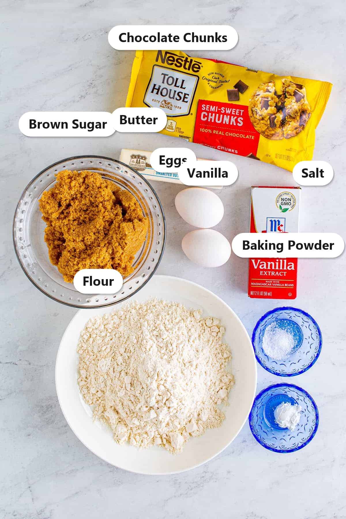 Labeled ingredients for chocolate chunk blondies including chocolate chunks, brown sugar, butter, eggs, vanilla, flour, baking powder, and salt.