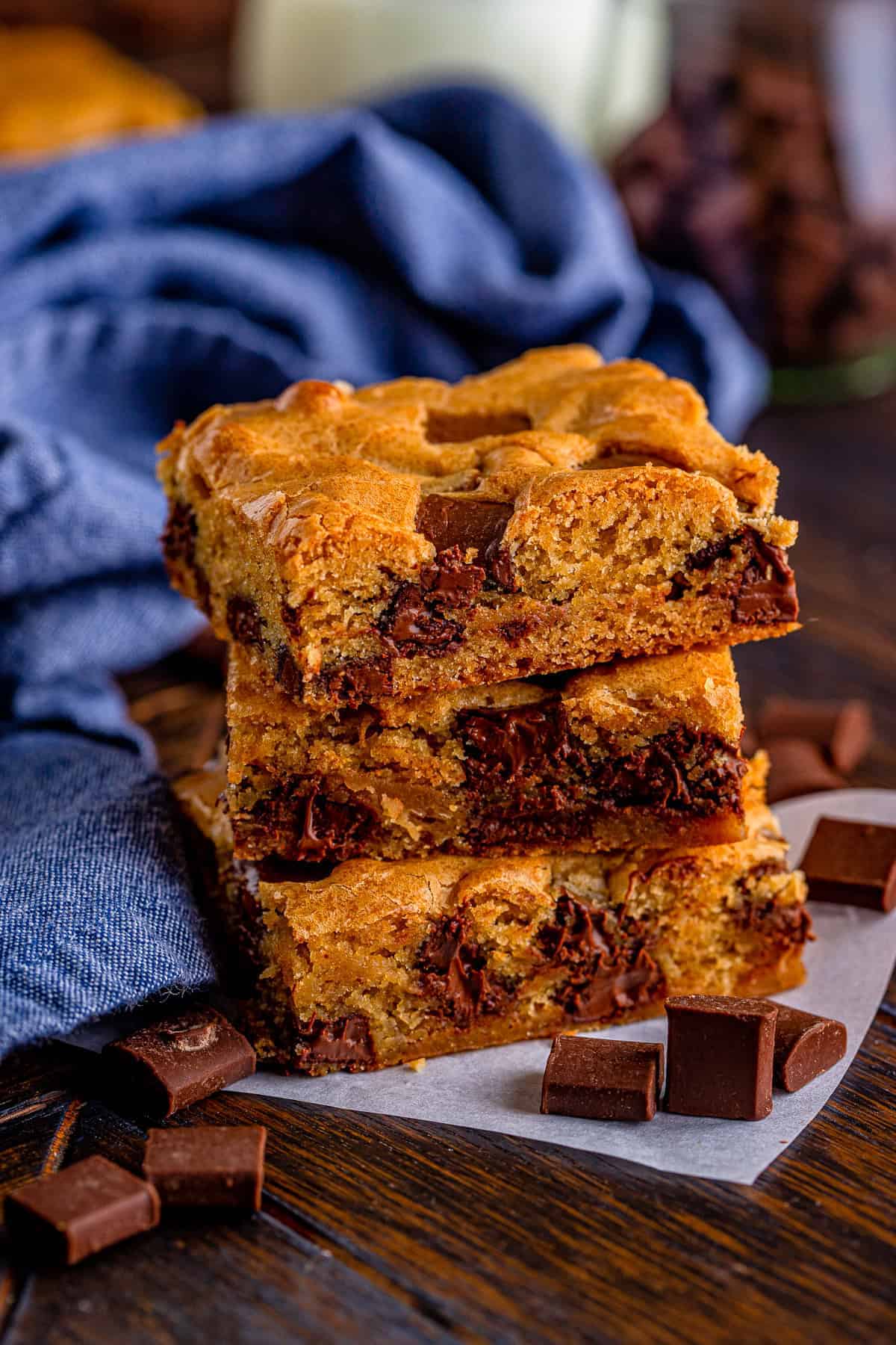 A stack of thick chocolate chunk blondies on parchment paper with chocolate chunks scattered around.