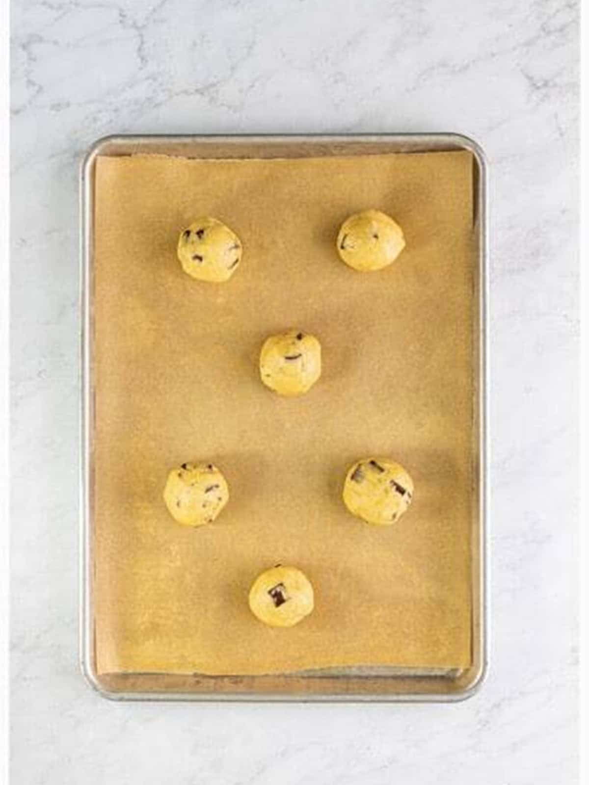 Balls of cookie dough rolled and placed on a parchment-lined baking sheet.