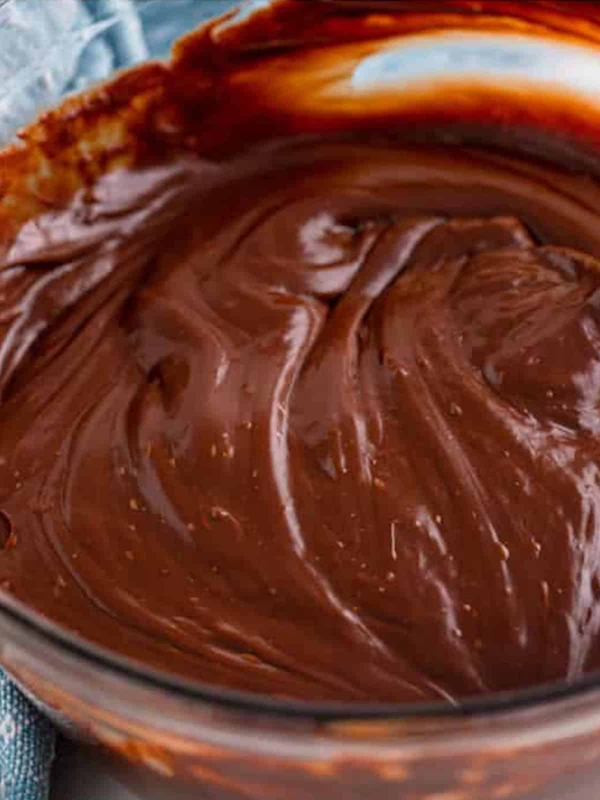 Melted, smooth chocolate fudge stirred together in a glass bowl.