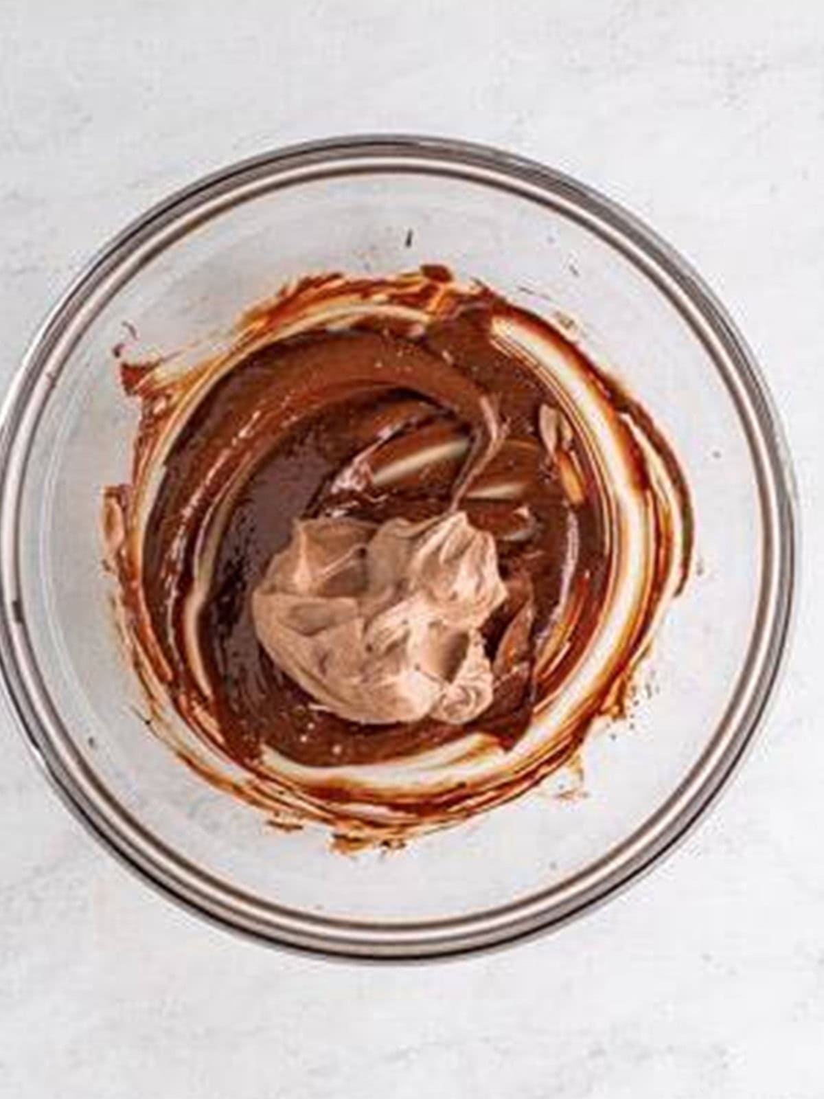Folding melted chocolate into whipped cream to make chocolate mousse.