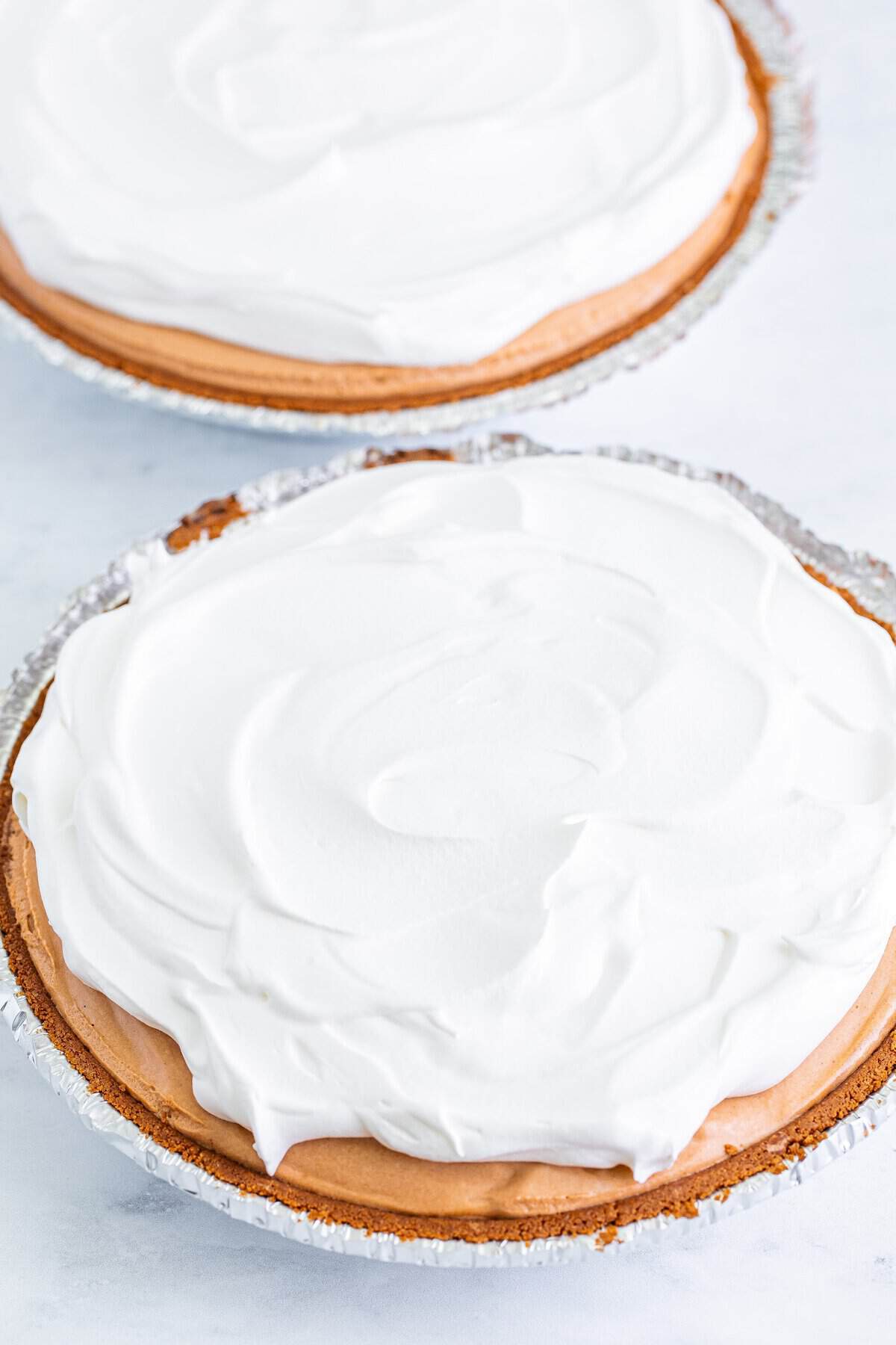 No bake chocolate peanut butter pie topped with whipped cream before chilling.