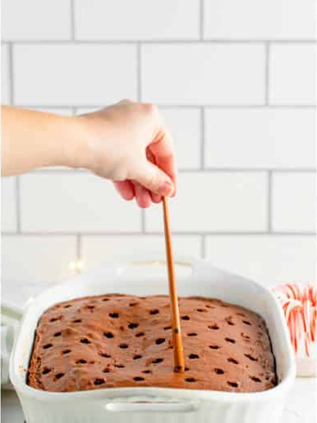 Poking holes all over the warm chocolate cake with a utensil.