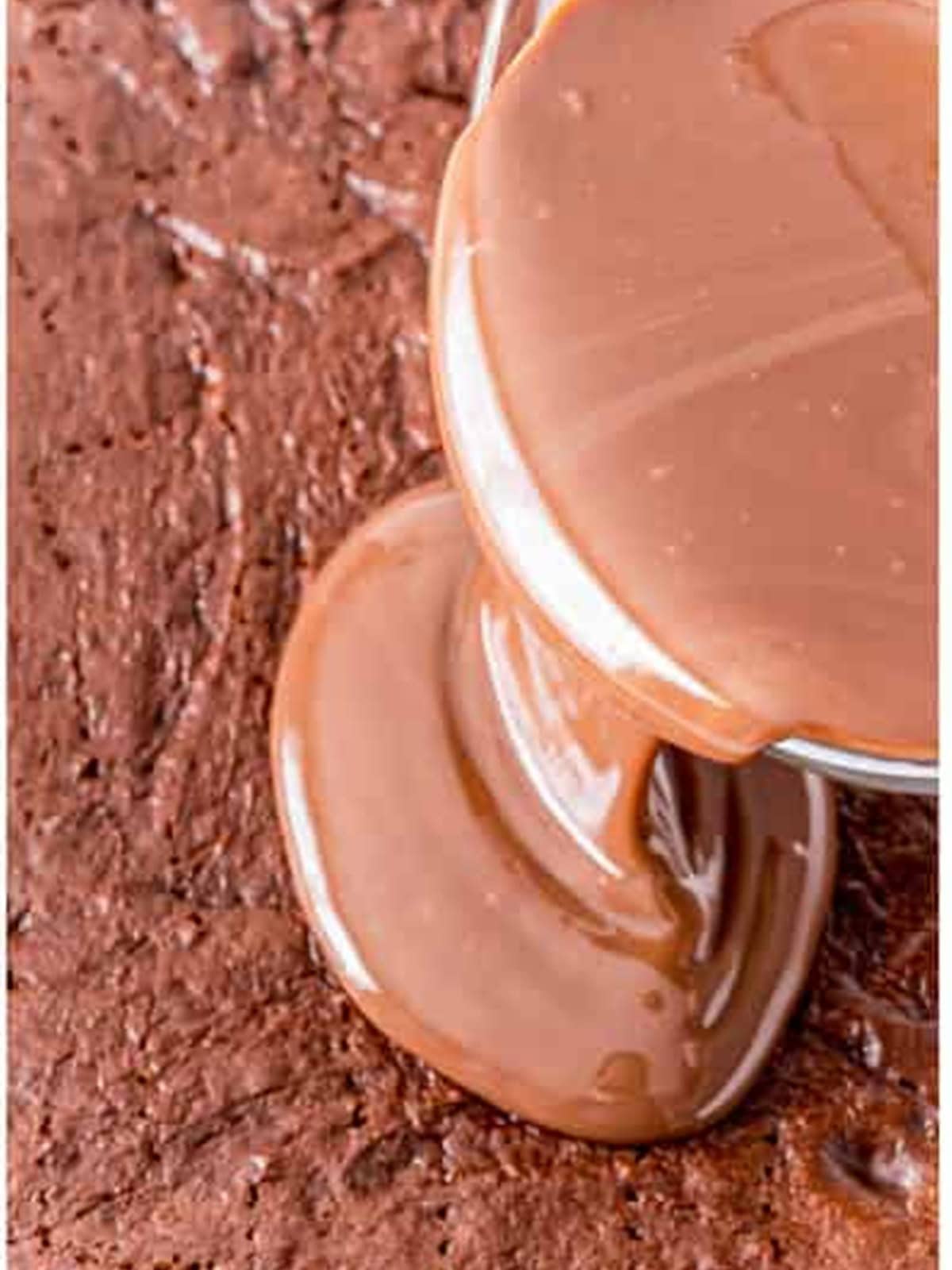 Pouring sweetened condensed milk and chocolate filling over a poked chocolate cake.