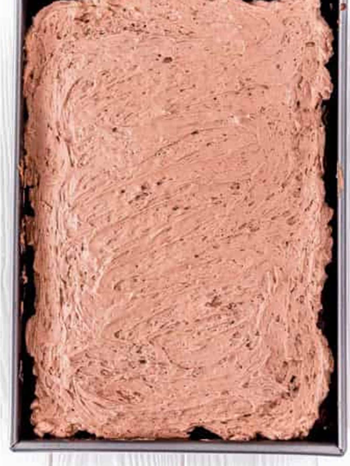 Spreading chocolate whipped cream frosting over a chocolate poke cake.