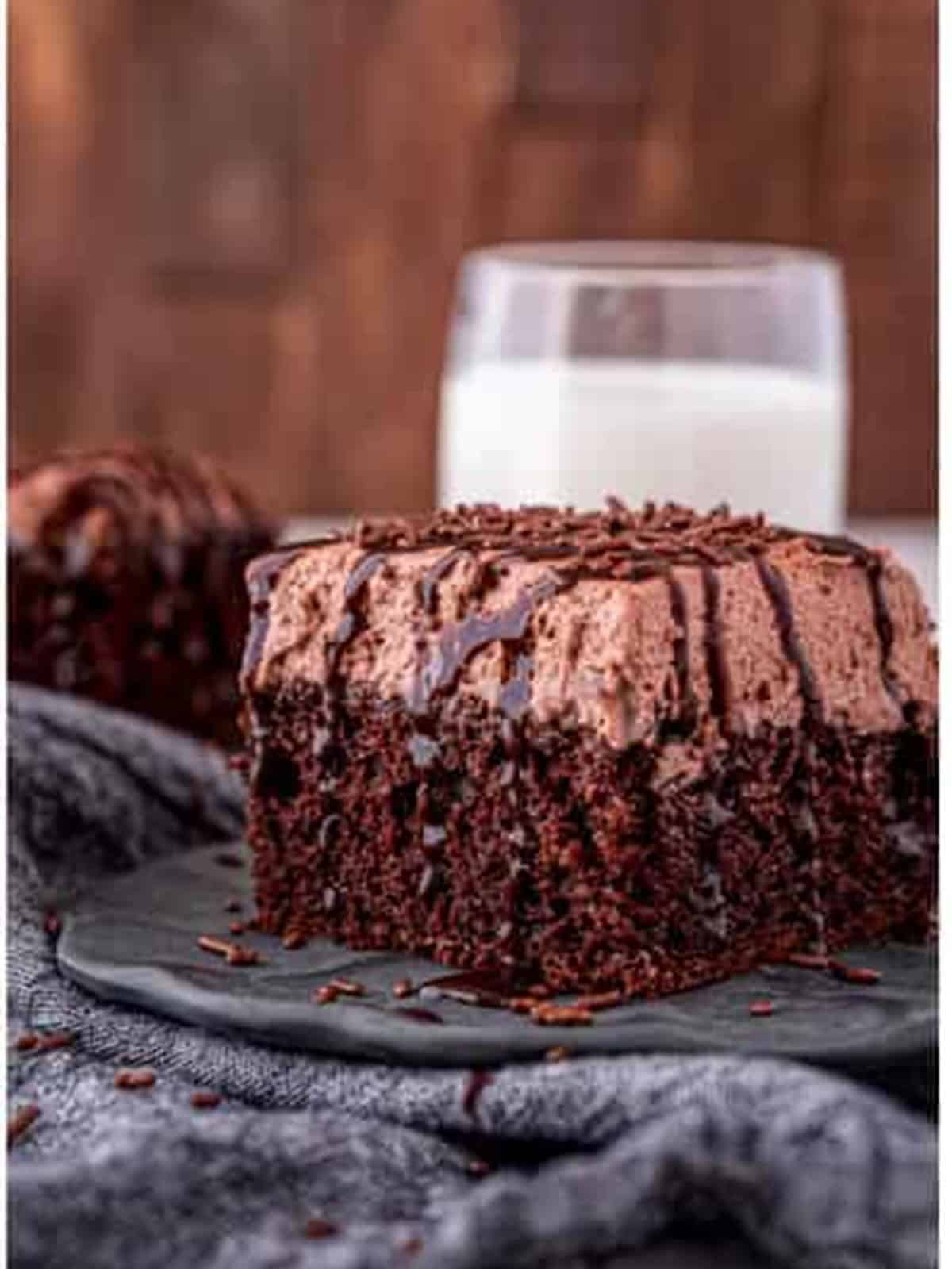 A slice of finished chocolate poke cake on a plate with a glass of milk.