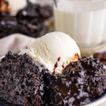 A scoop of warm chocolate pudding cake topped with vanilla ice cream on a plate.
