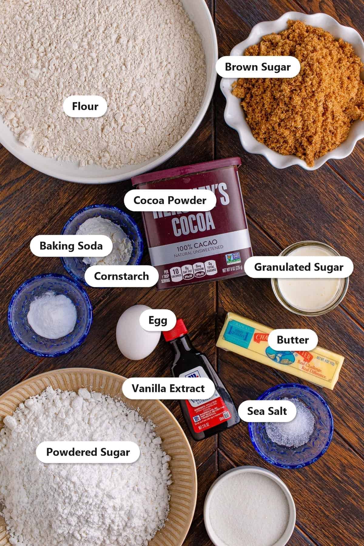 Labeled ingredients for chocolate sugar cookies including flour, cocoa powder, brown sugar, butter, egg, vanilla, and powdered sugar for frosting.