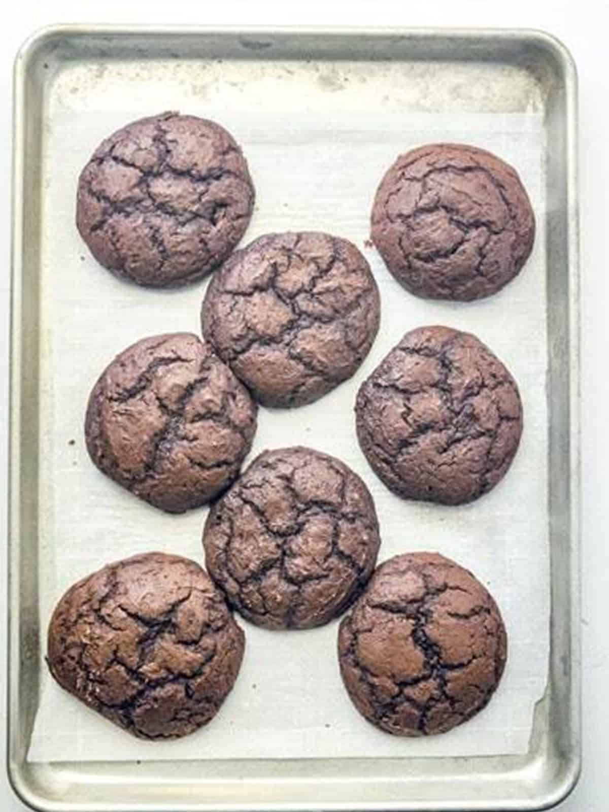 Baked chocolate whoopie pie cookies cooling on a baking sheet.