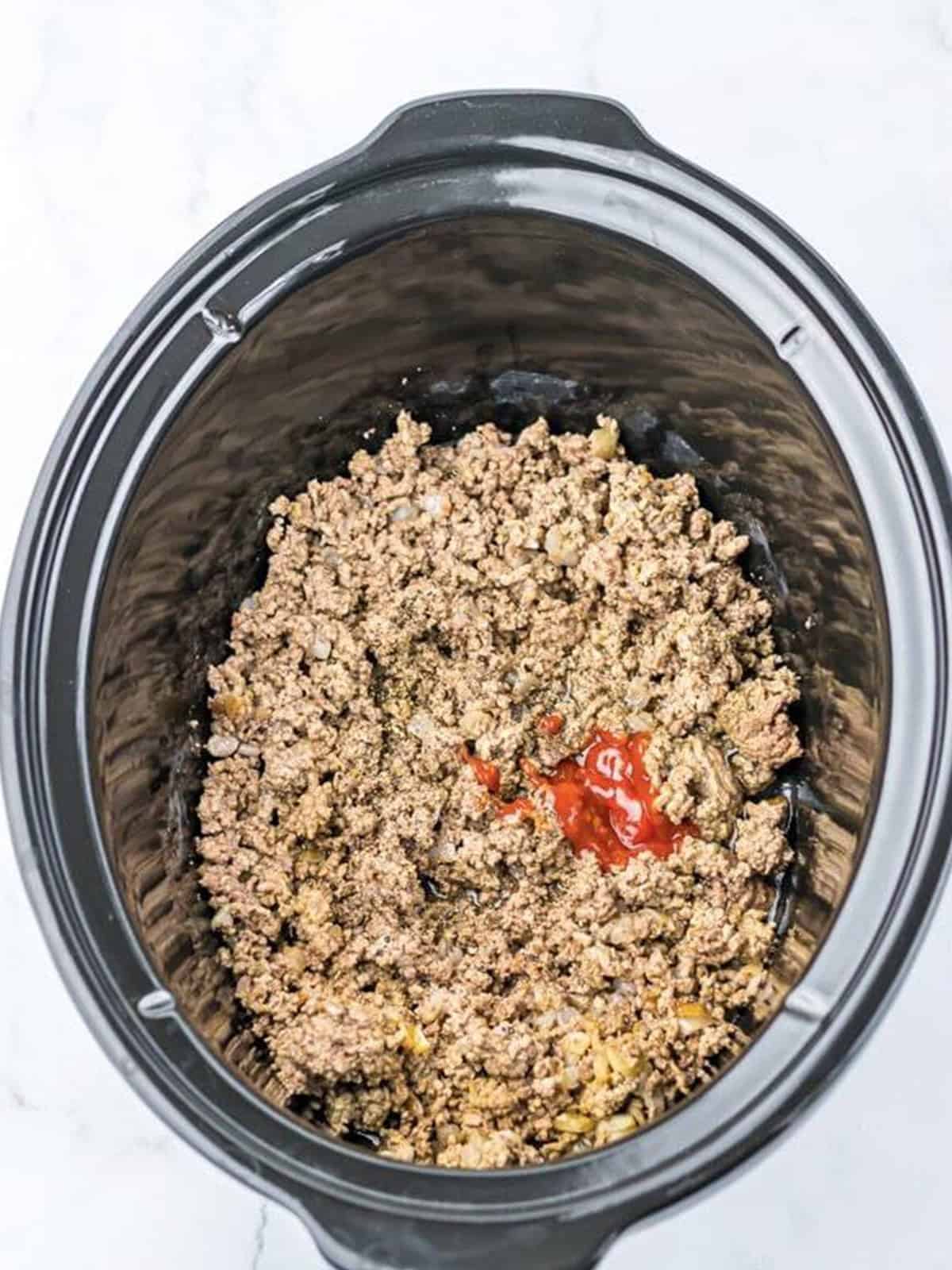 Ground beef and onion browned in a slow cooker for chopped cheese sandwiches.