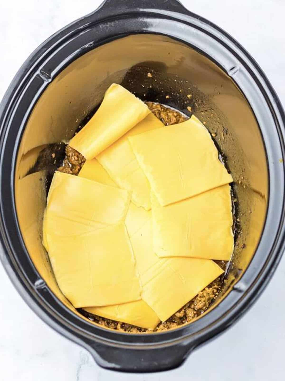 American cheese slices layered over the cooked beef in a slow cooker.