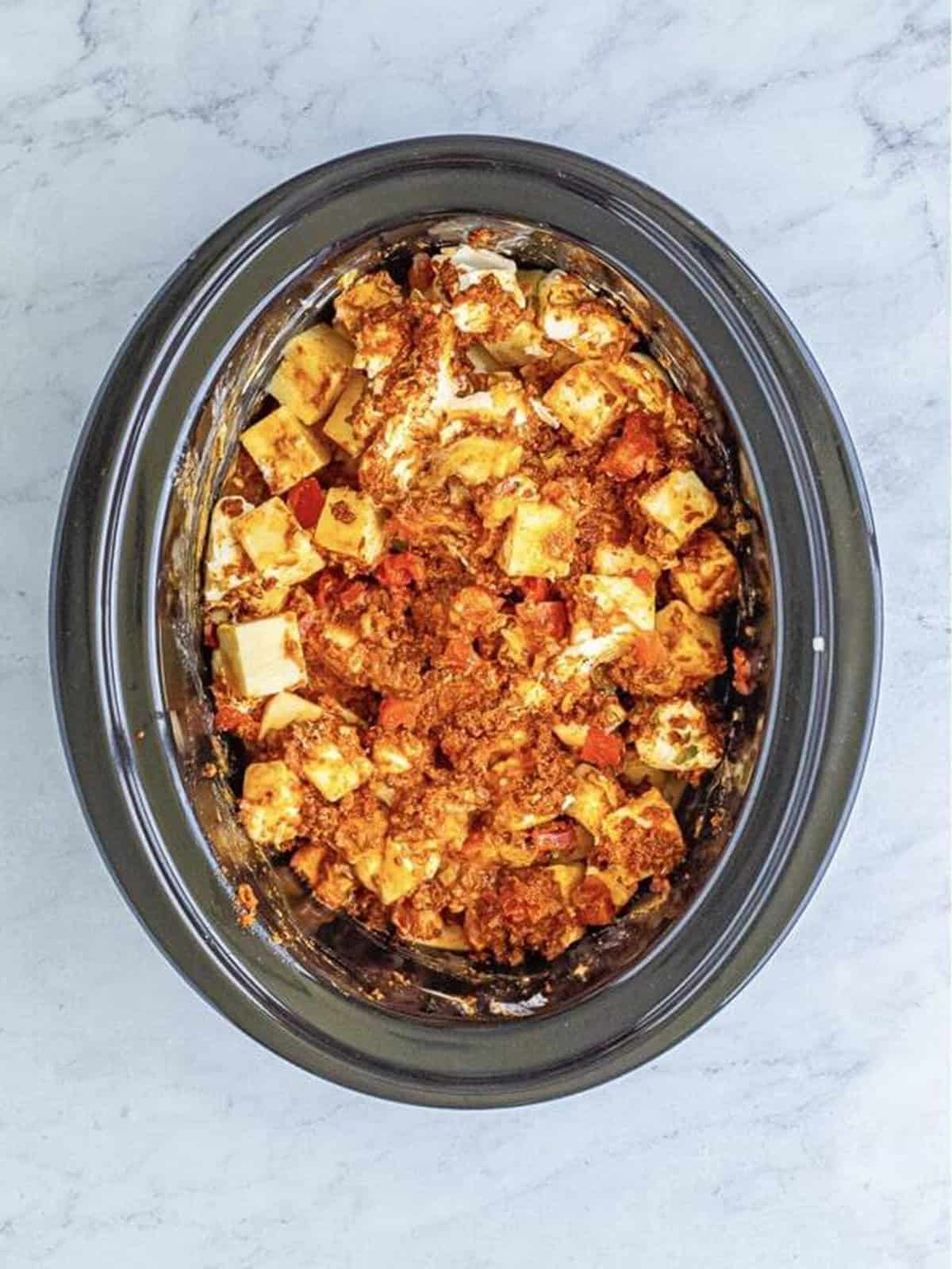 Chorizo and cheese cubes stirred together in the slow cooker.