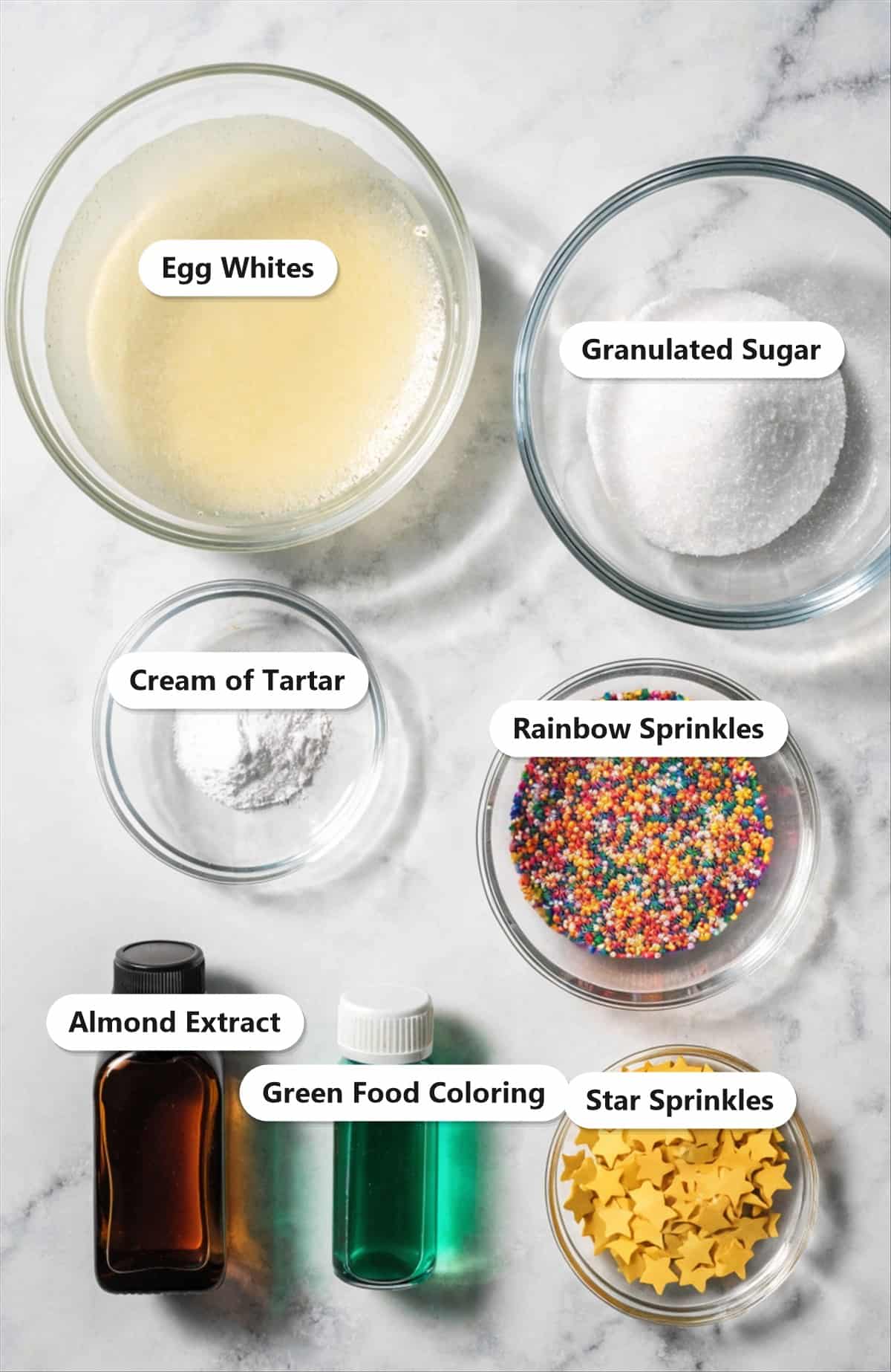 Labeled ingredients for Christmas tree meringue cookies including egg whites, granulated sugar, cream of tartar, almond extract, green food coloring, and sprinkles.