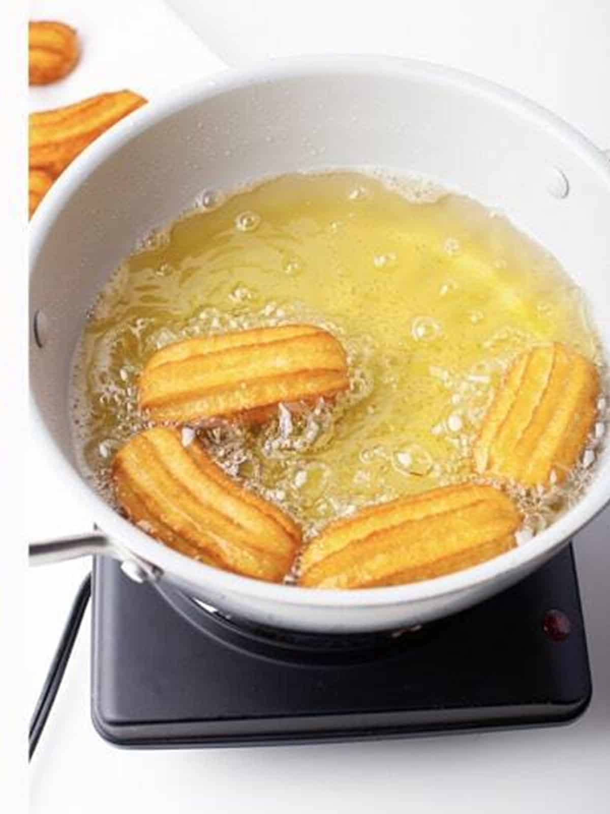 Mini churros piped into hot oil and frying until golden brown.
