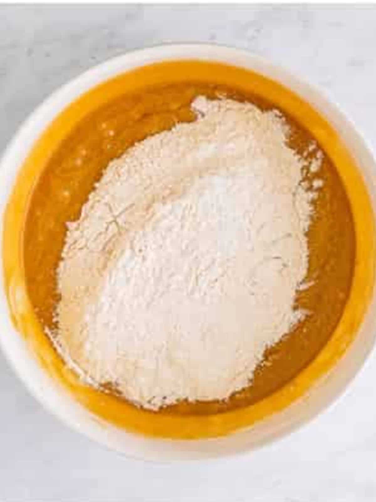 Flour added to the blondie batter in a white bowl.