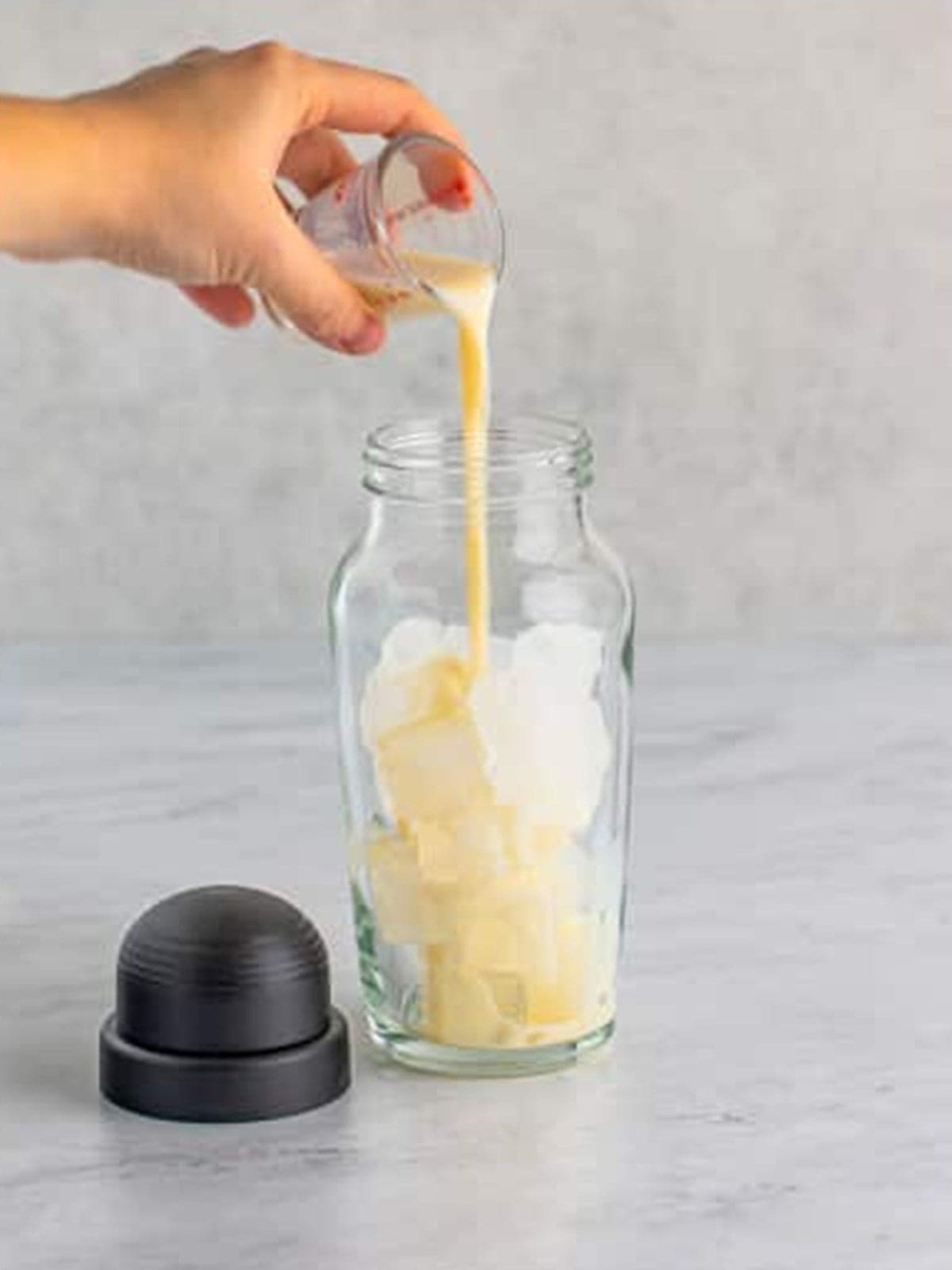 RumChata poured into the cocktail shaker over ice for cinnamon roll cocktail.