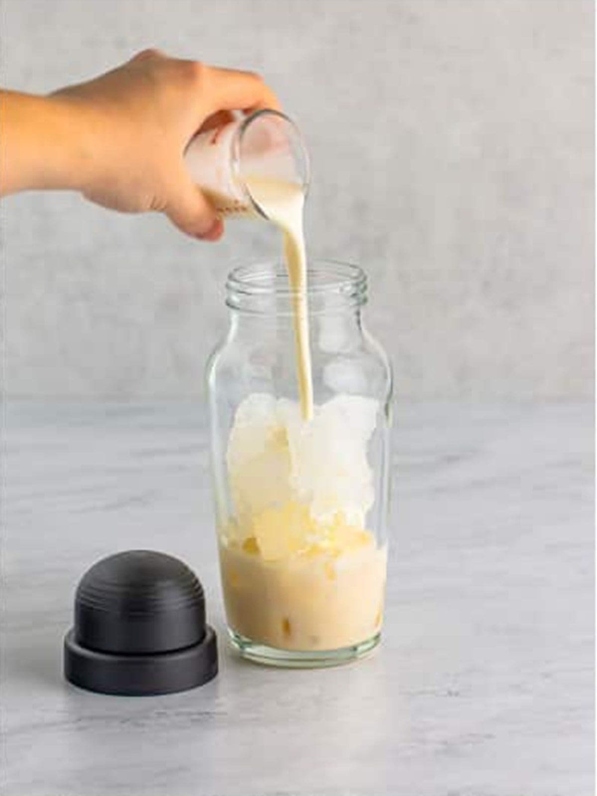 Heavy cream poured into the cocktail shaker for cinnamon roll cocktail.