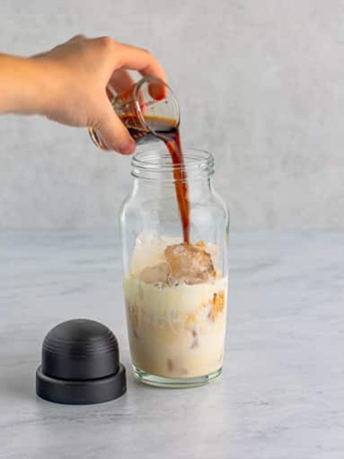 Kahlua coffee liqueur poured into the shaker for cinnamon roll cocktail.