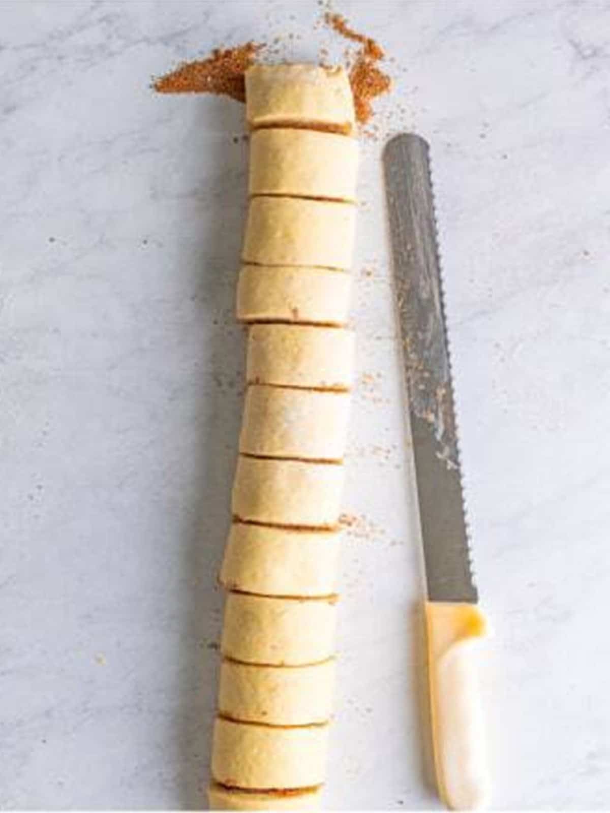A log of cinnamon roll dough being cut into even rolls with a serrated knife.