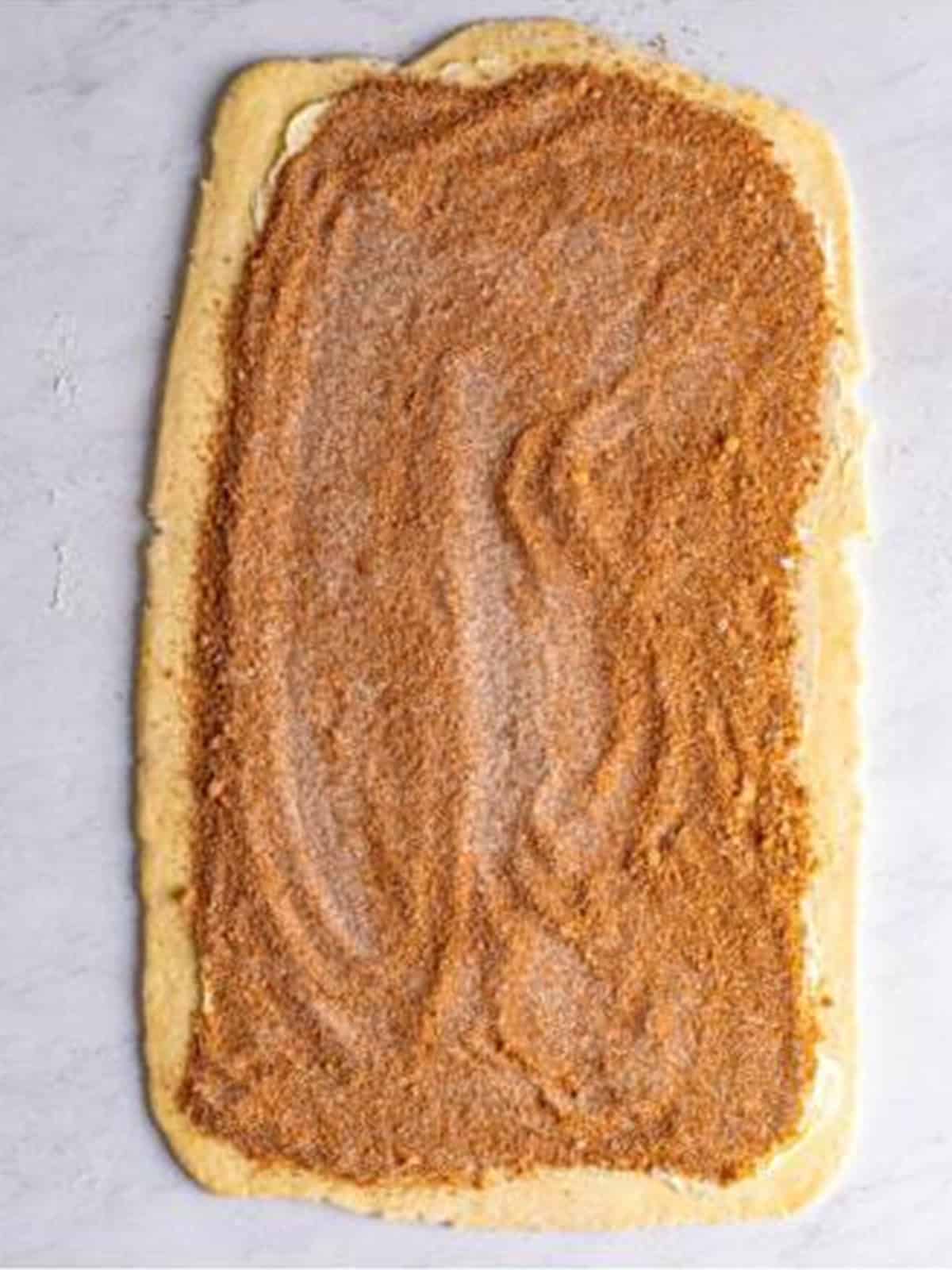 Cinnamon sugar filling spread over the rolled out cinnamon roll dough.