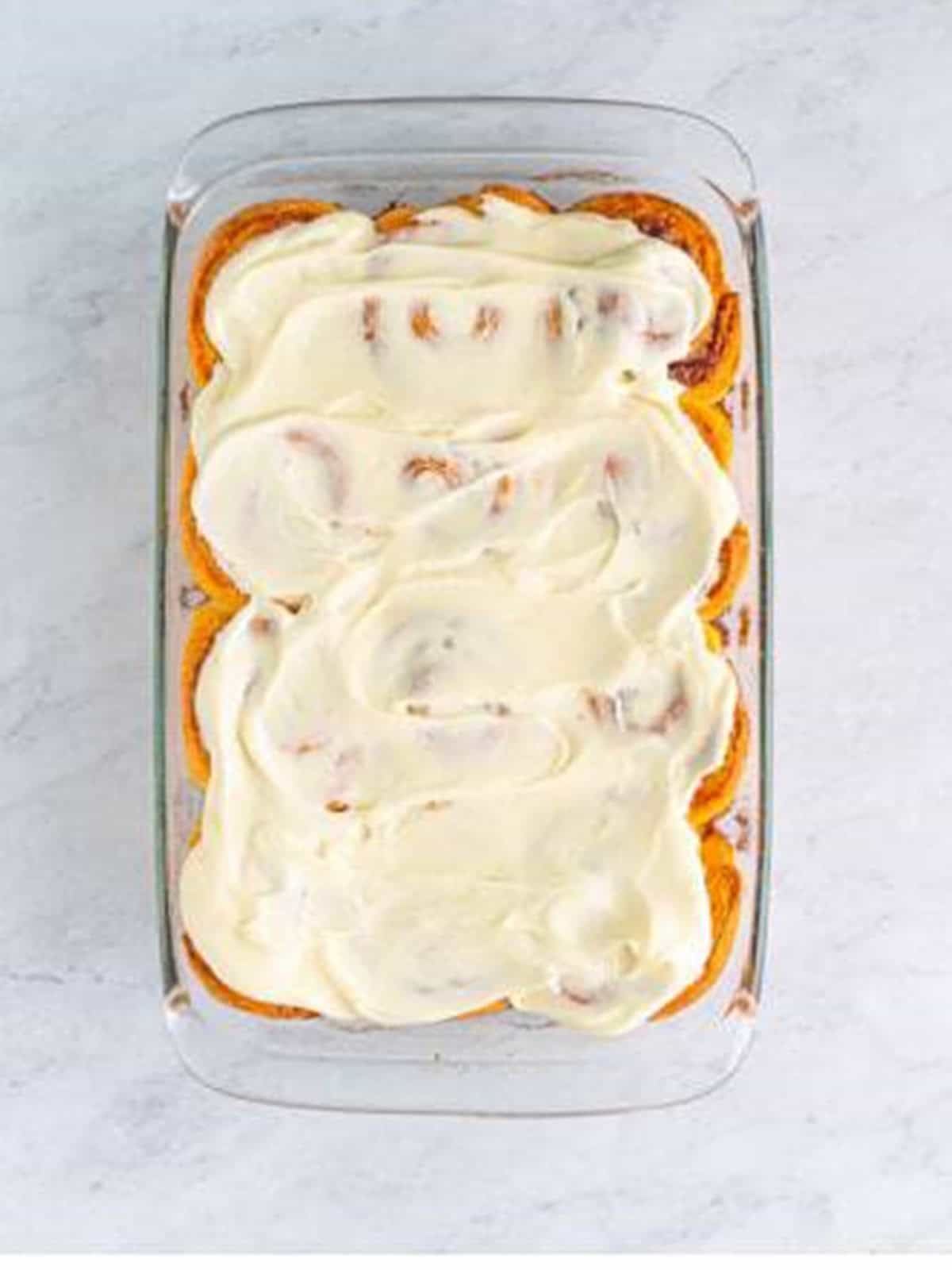 Baked cinnamon rolls topped with cream cheese frosting in the pan.