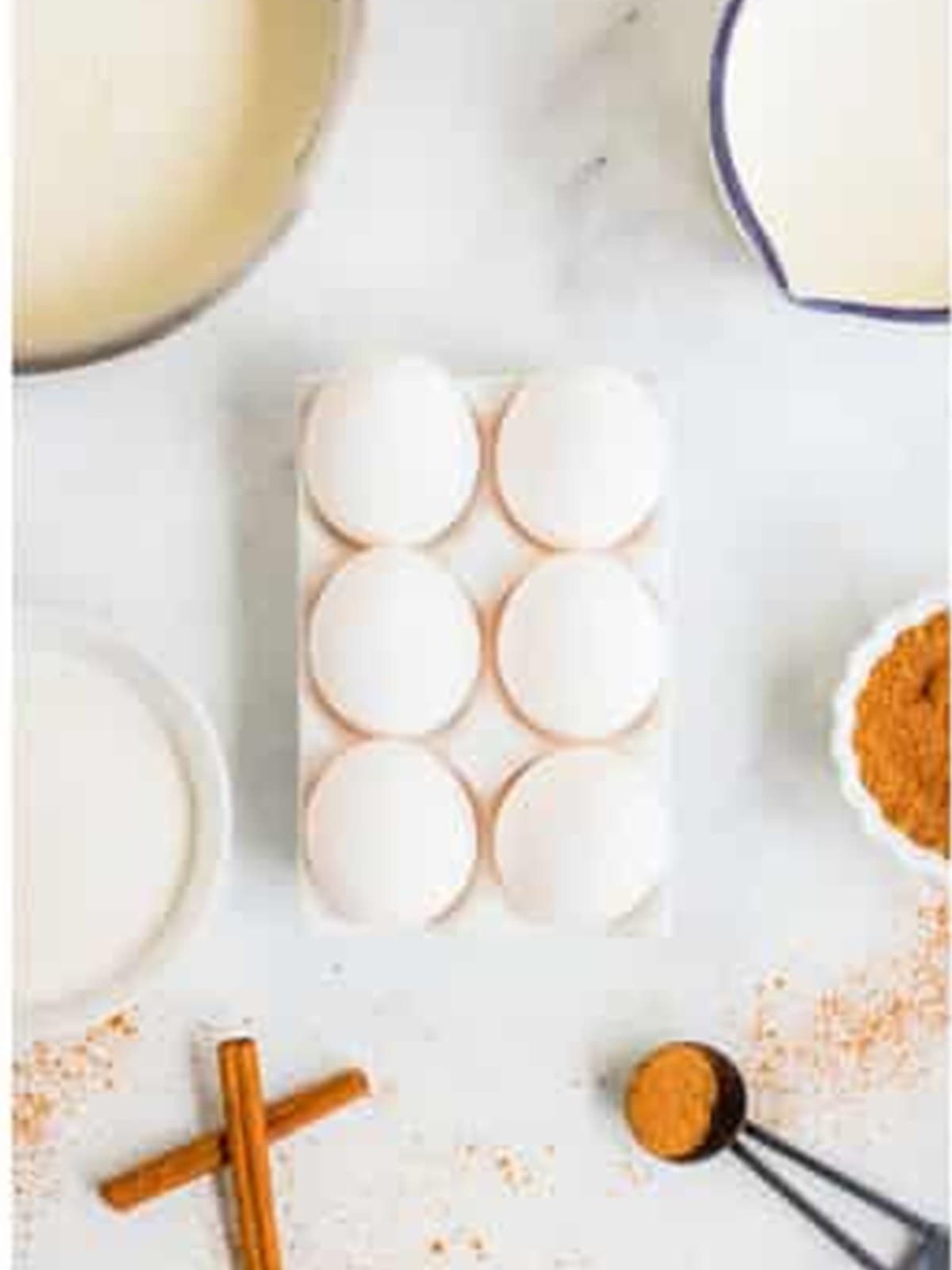 Eggnog ingredients including whole milk, eggs, nutmeg, and cinnamon on a marble counter.