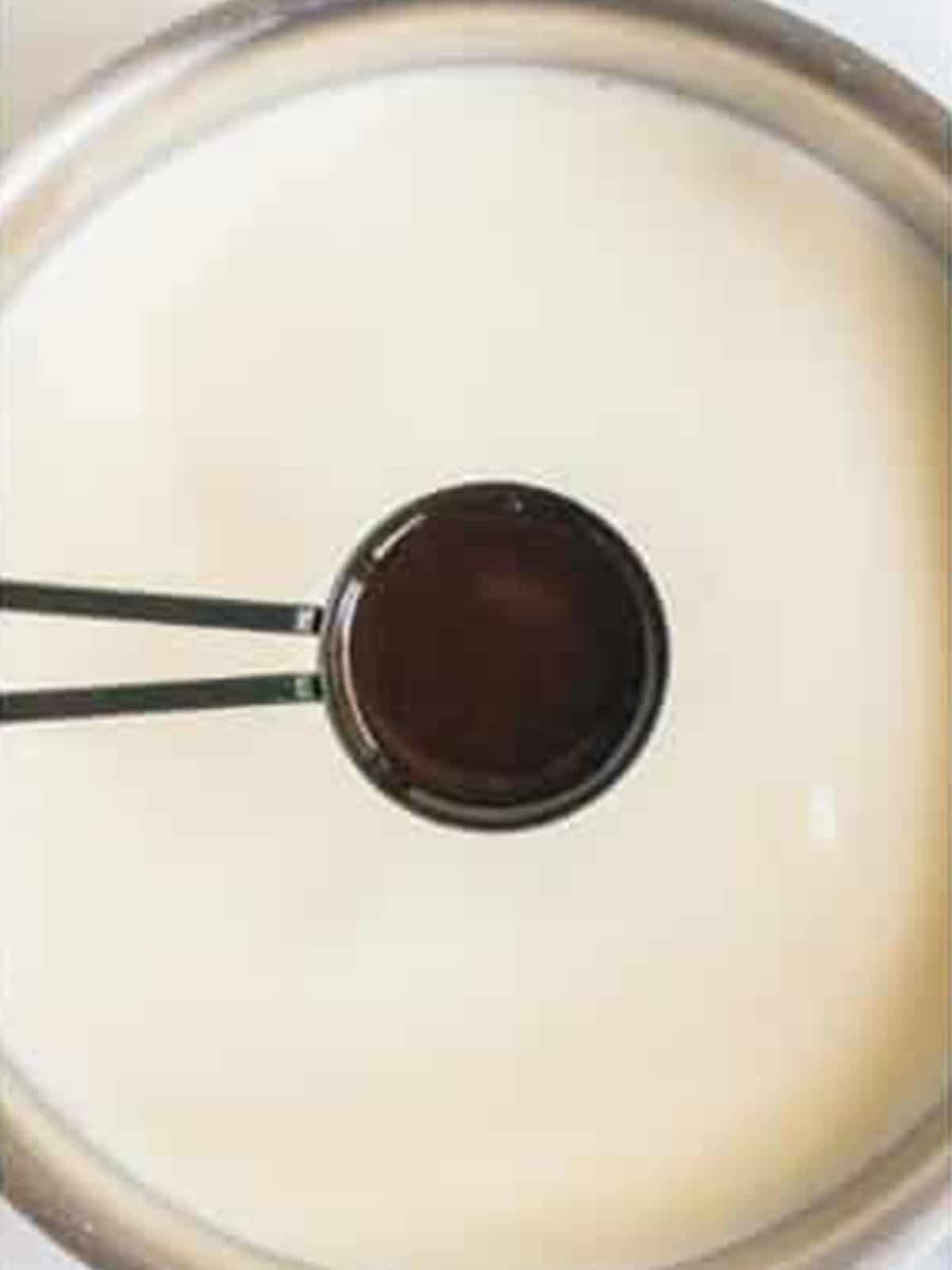 Vanilla extract being whisked into warm milk in a saucepan for eggnog.