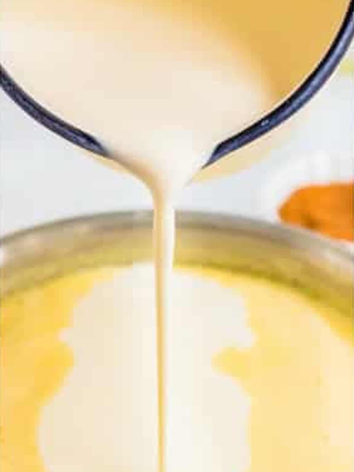 Egg mixture being poured into the saucepan of warm milk for eggnog.