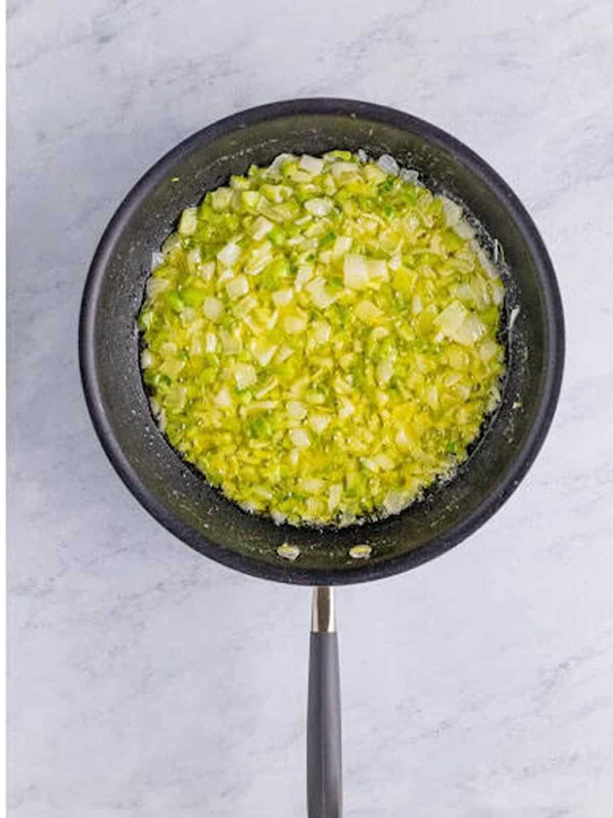 Chopped celery and onion cooking in melted butter in a skillet for stuffing.