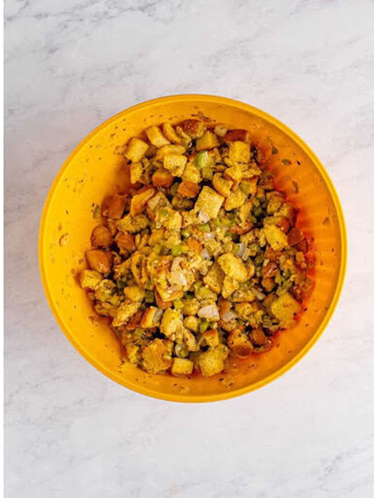 White bread cubes tossed with the cooked vegetable mixture in a large bowl.