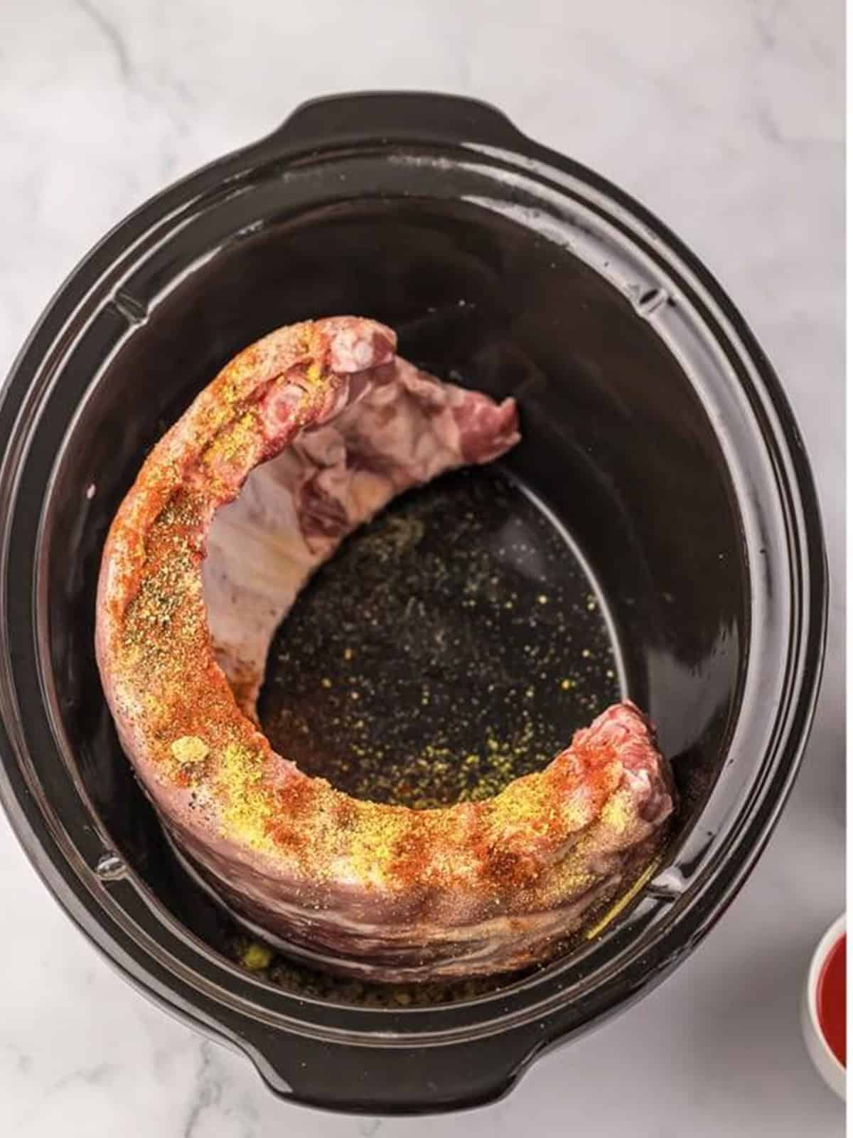 Baby back ribs seasoned with spices in a slow cooker.