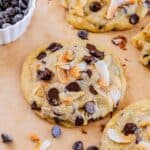 Coconut chocolate chip cookies on parchment scattered with chocolate chips and coconut flakes.
