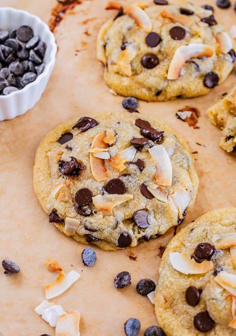 Coconut chocolate chip cookies on parchment scattered with chocolate chips and coconut flakes.