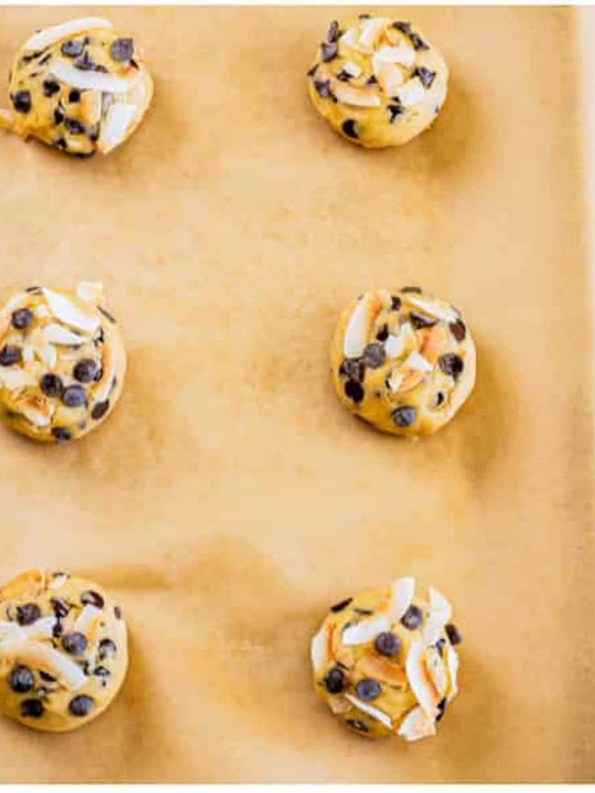 Coconut chocolate chip cookie dough rolled into balls on a parchment lined tray.