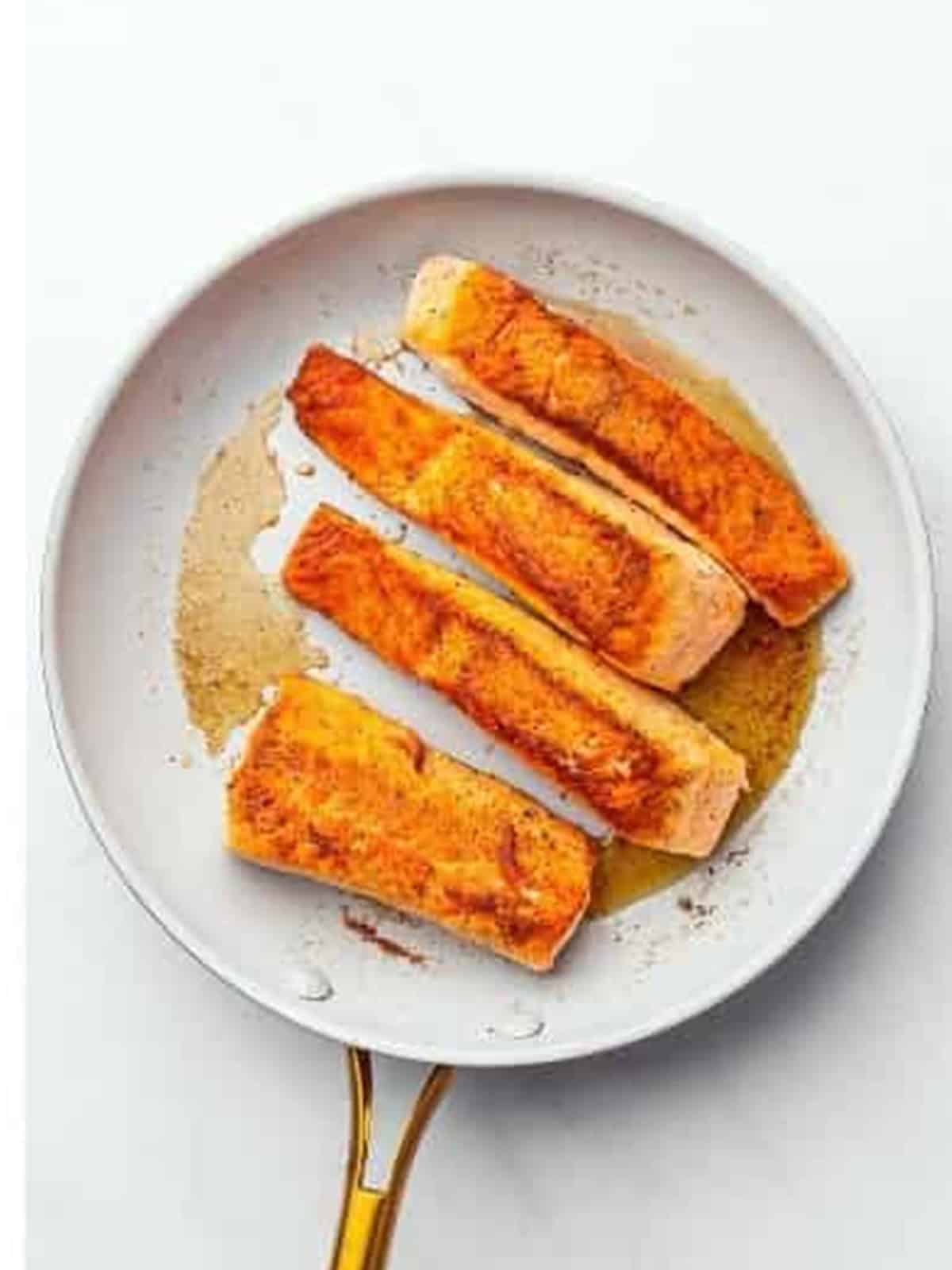 Golden seared salmon fillets flipped and cooked through in the pan.