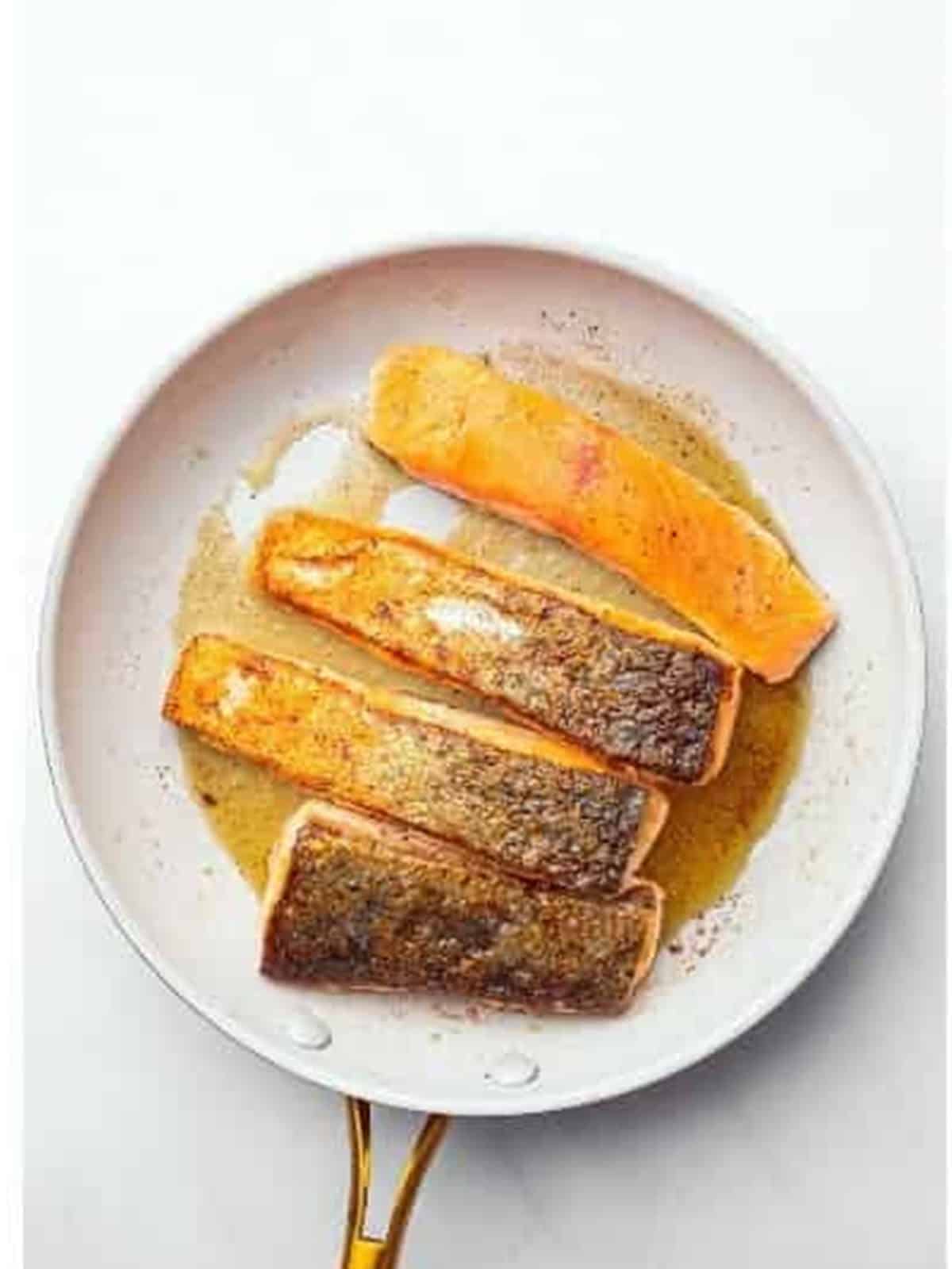 Salmon fillets searing skin-side down in a buttered pan.