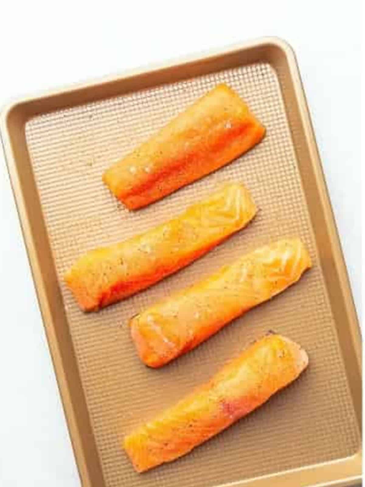 Seasoned salmon fillets on a sheet tray ready to be seared.