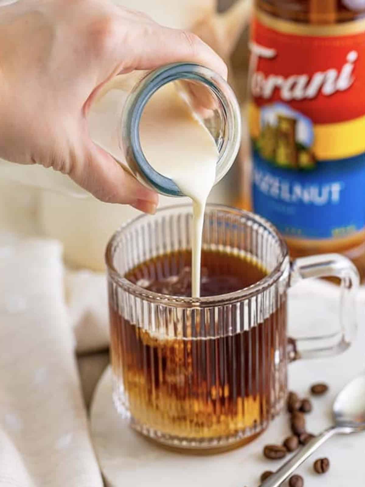 Pouring hot coffee and cream into a mug with coffee syrup.