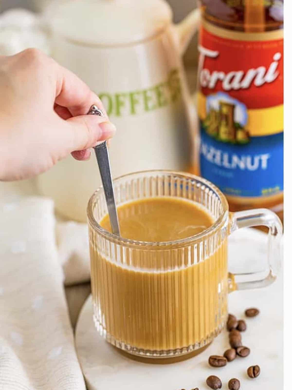 Stirring a flavored hot latte made with coffee syrup.