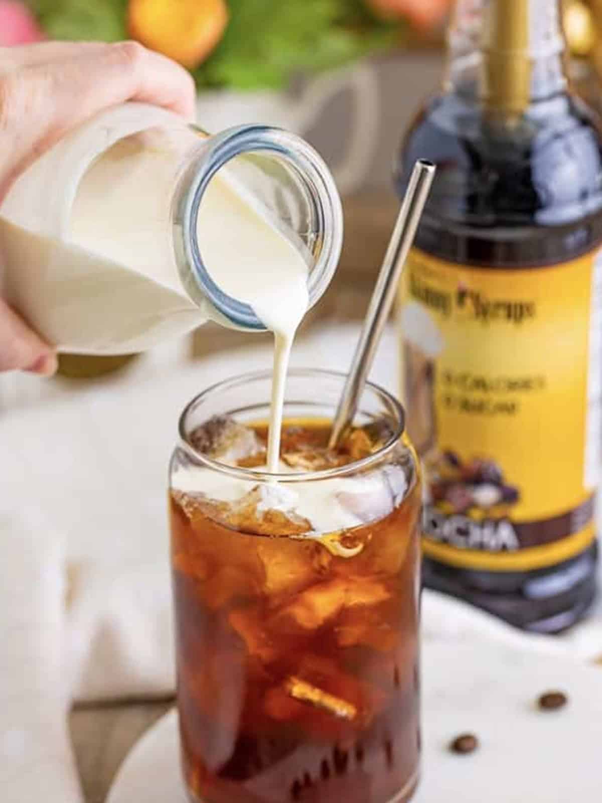 Adding coffee syrup and cold coffee to a glass of ice.