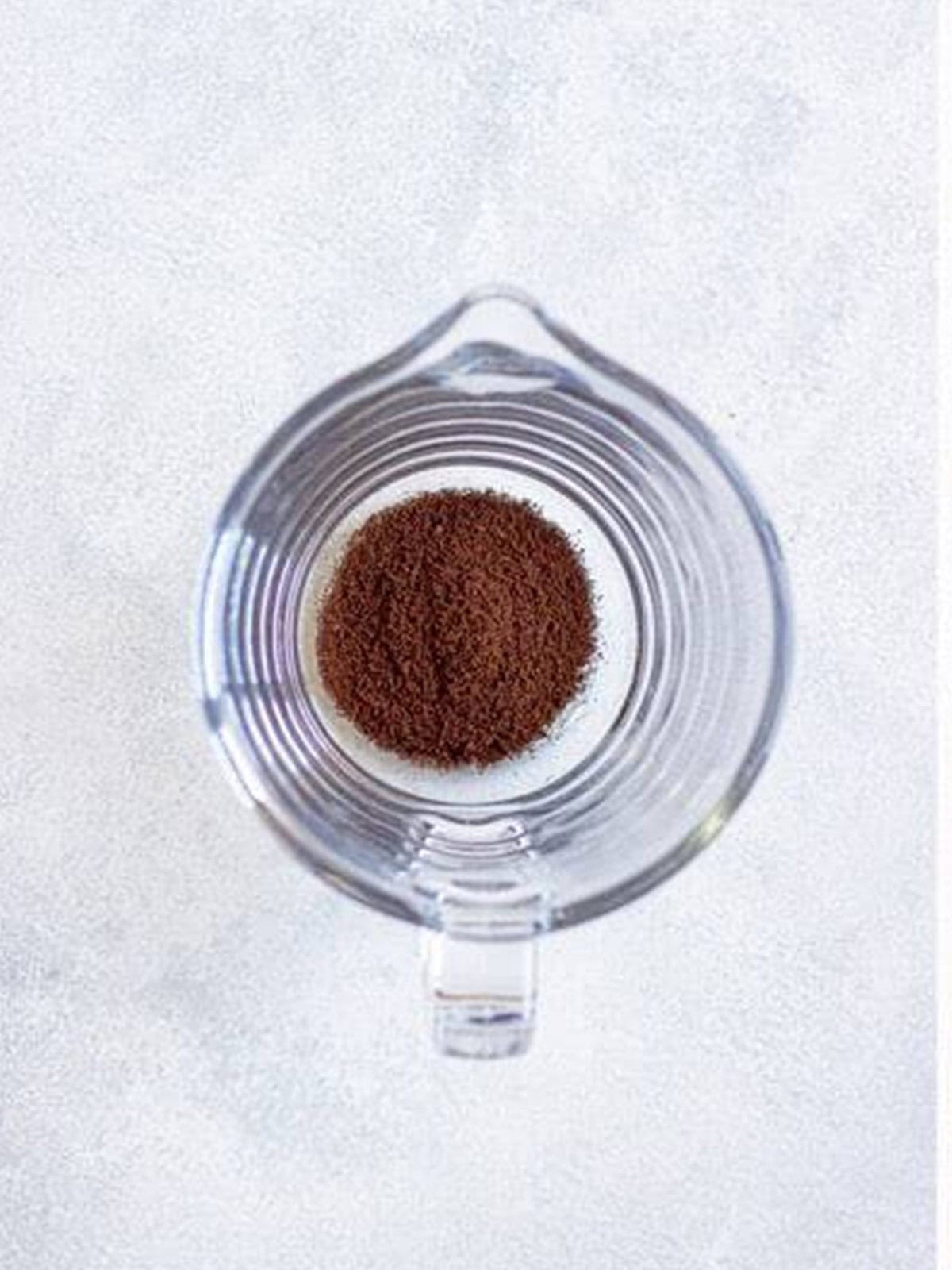Coarse coffee grounds added to the bottom of a glass pitcher.