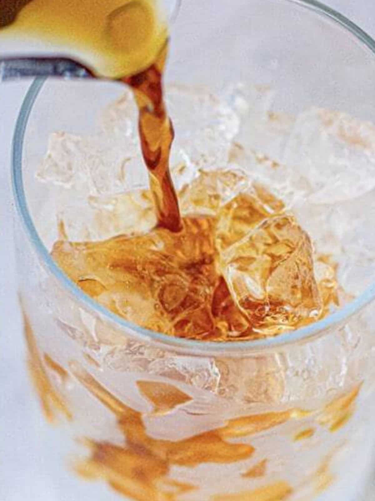 Cold brew coffee being poured over a glass of ice.
