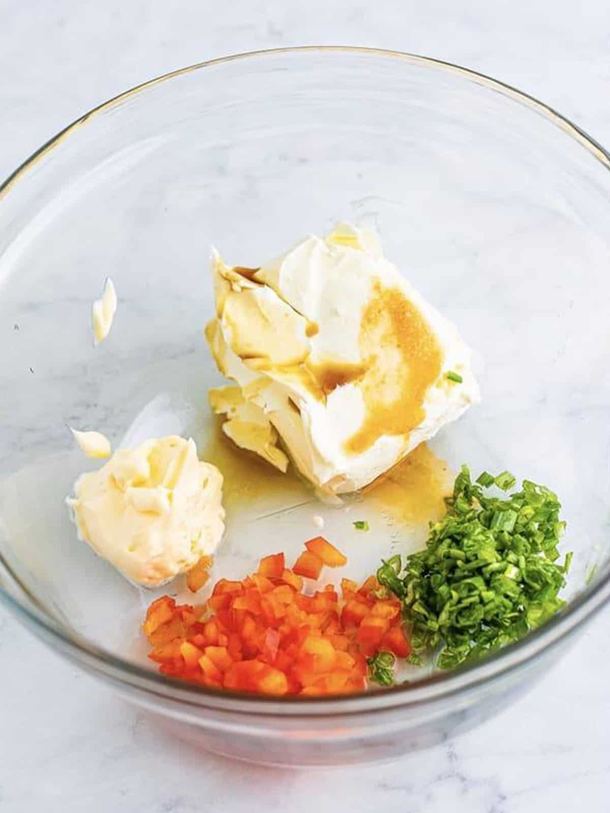 Cream cheese, mayonnaise, scallions, and seasonings in a glass mixing bowl for cold crab dip recipe.