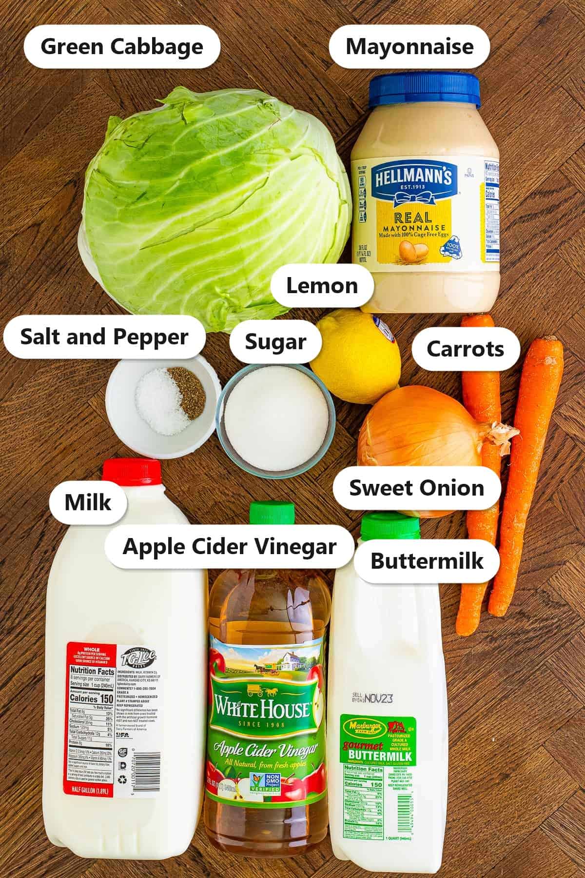 Coleslaw ingredients including green cabbage, mayonnaise, buttermilk, sugar, carrots, sweet onion, lemon, milk, and apple cider vinegar on a wood board.