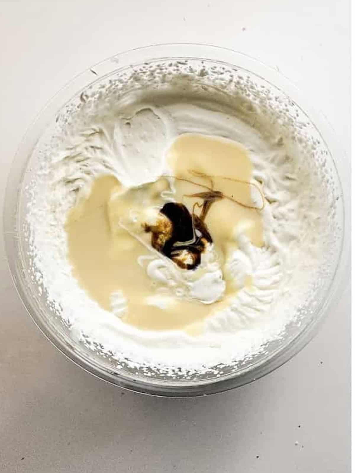 Heavy whipping cream whipped to soft peaks in a stand mixer bowl for no-churn cookie monster ice cream.