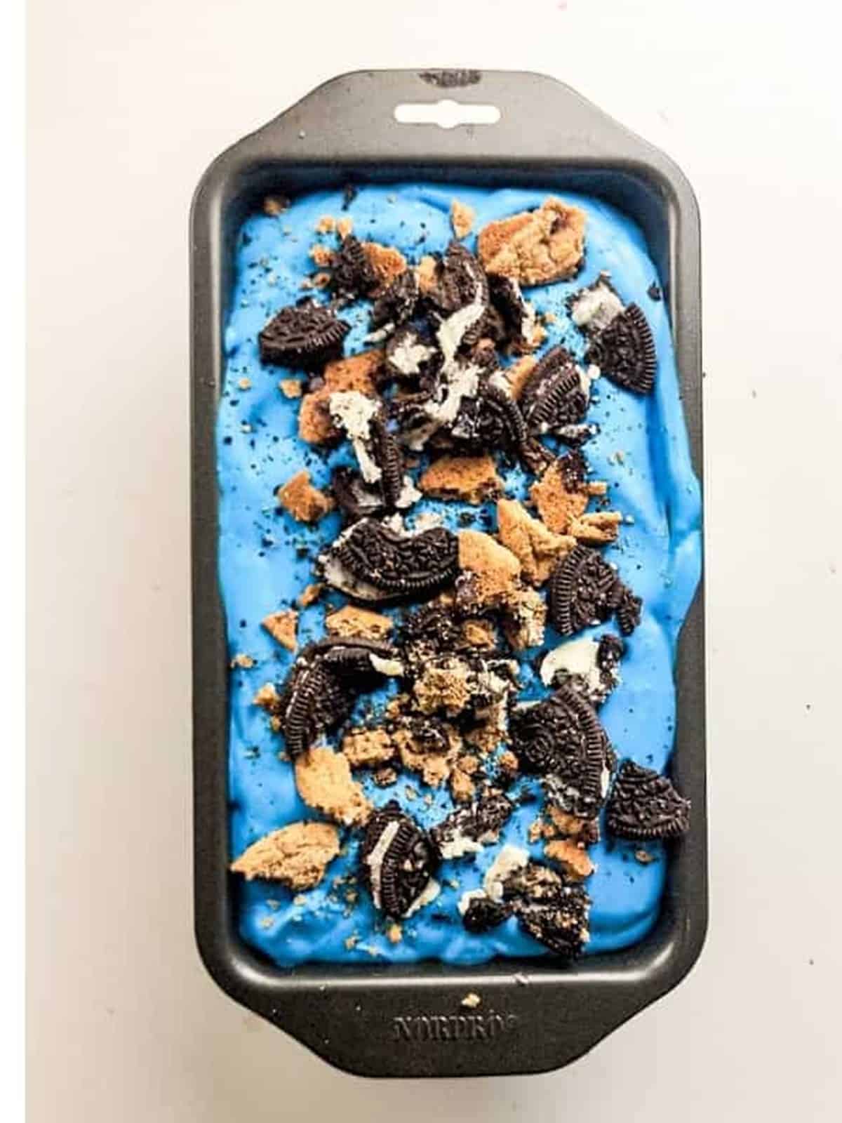 Blue cookie monster ice cream spread into a loaf pan and topped with extra chopped cookies before freezing.