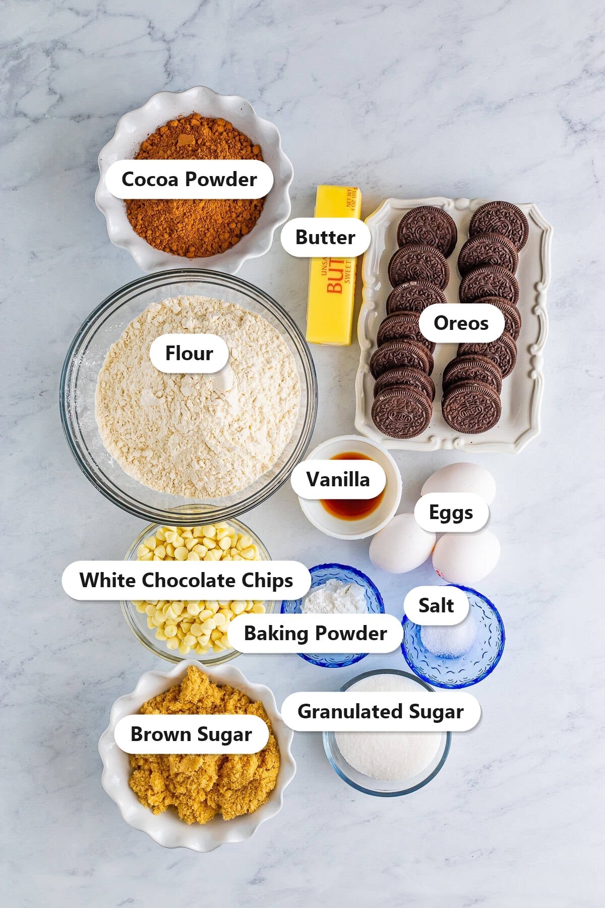 Labeled ingredients for cookies and cream cookies including flour, cocoa powder, butter, Oreos, white chocolate chips, brown sugar, granulated sugar, eggs, and vanilla.