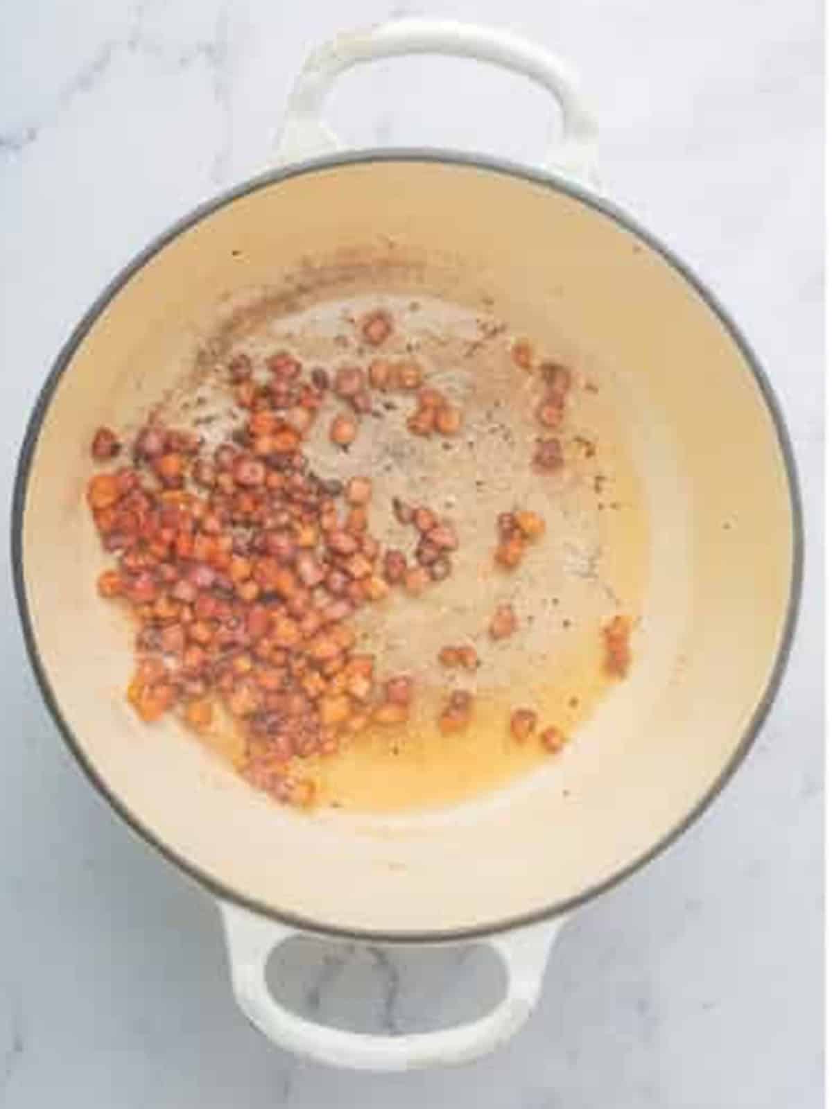 Cooking chopped bacon until crispy in a large white pot for corn chowder.